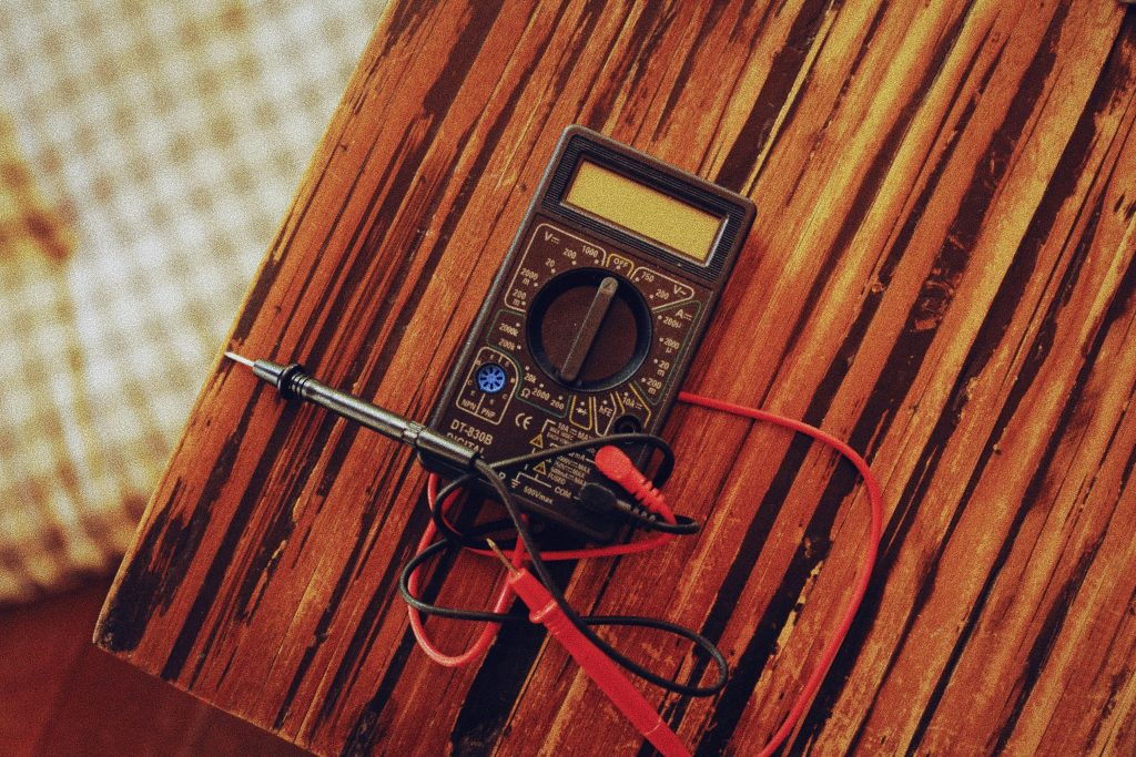 Digital multimeter with test probes resting on a wooden surface, representing electrical testing and safety checks in workplace environments